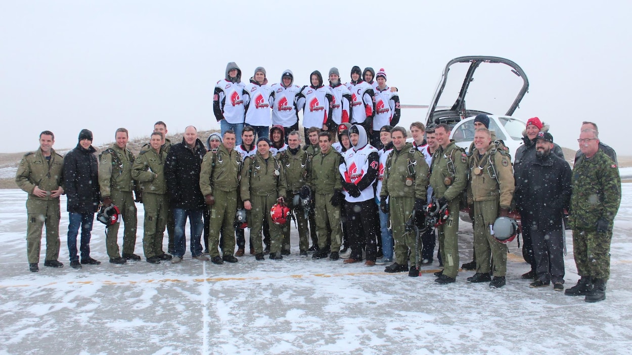 Des membres des Snowbirds posent avec des joueurs des Warriors devant un avion en plein hiver.