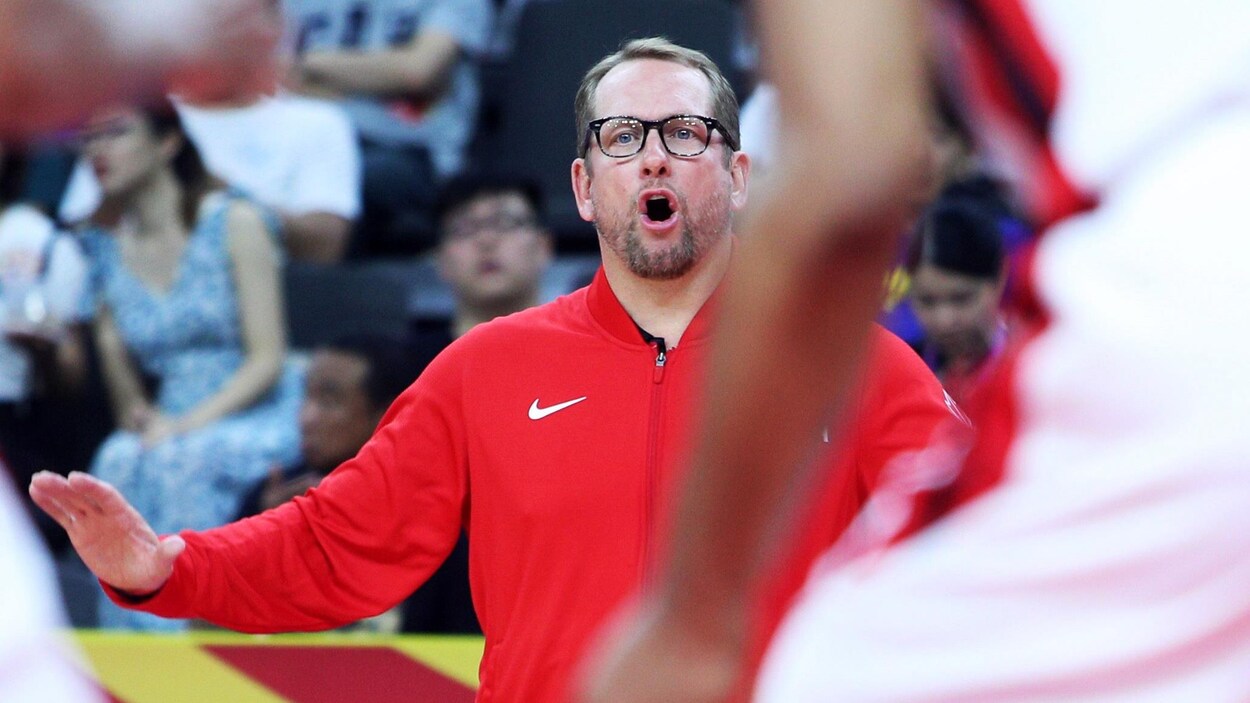 Debout sur les lignes de côté, il dirige les joueurs sur le parquet de basketball.