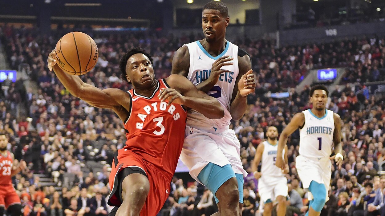 Il tient le ballon avec sa main droite et se défend contre Marvin Williams.