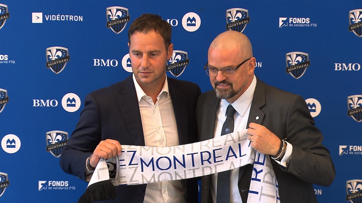 Deux hommes tiennent une bannière devant un mur bleu.
