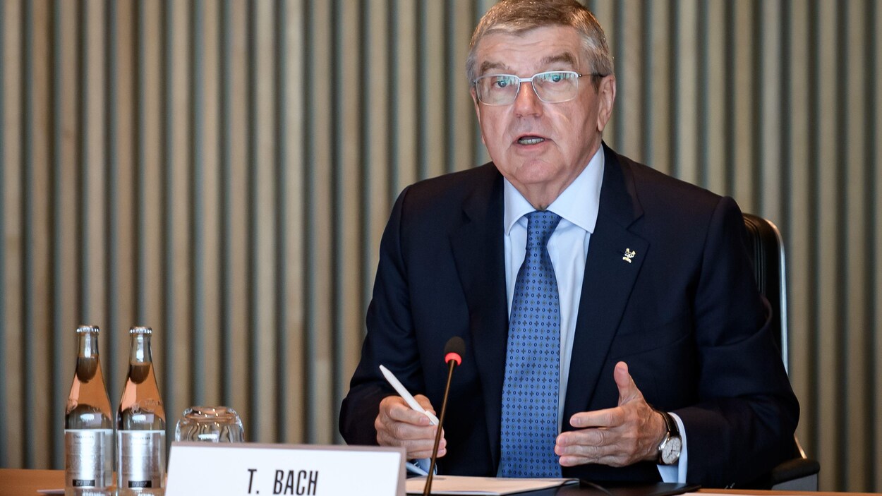 Il est assis devant une table en conférence de presse.
