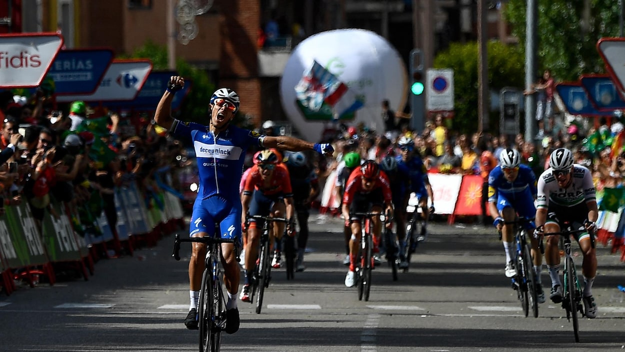 Un cycliste lève les bras en triomphe devant des adversaires qu'il vient de devancer au sprint.