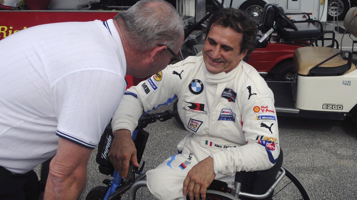 Alex Zanardi, assis dans une chaise roulante, discute avec quelqu'un dans le paddock du circuit automobile de Daytona, en marge d'essais pour la course de 24 heures.