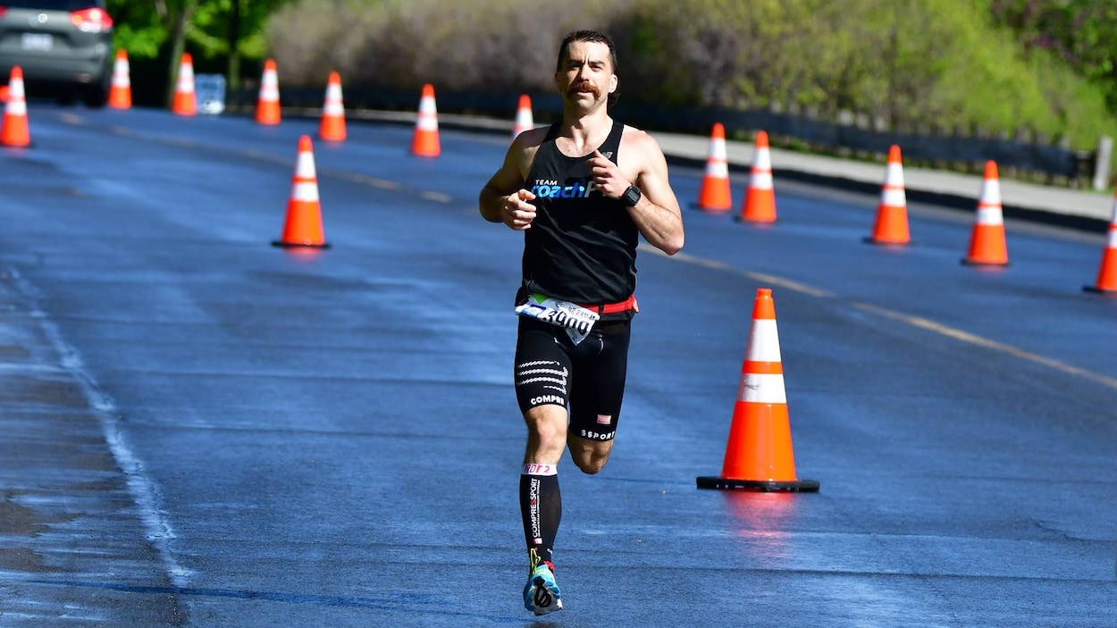Un coureur vêtu de noir court sur un parcours délimité par des cônes orange.