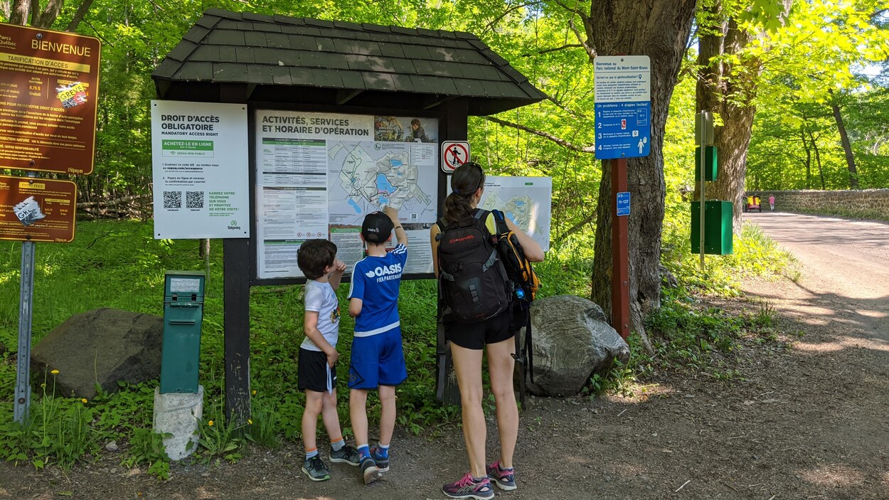 Une mère et ses deux fils se tiennent devant des pancartes.