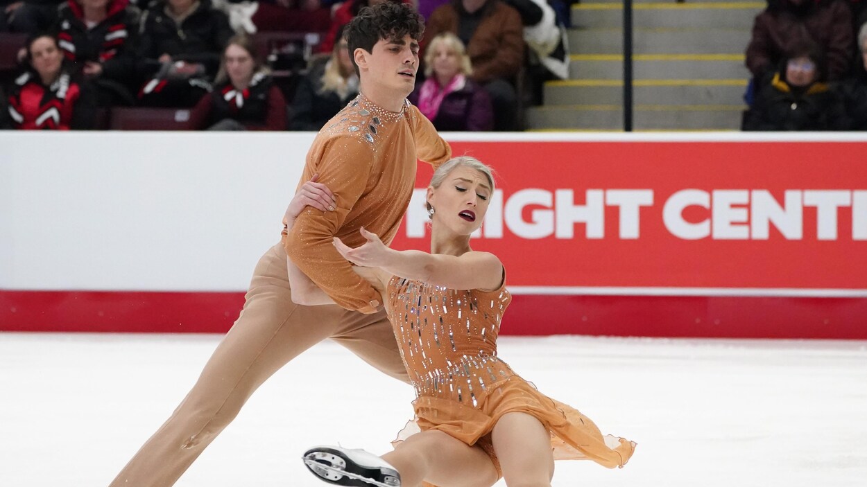 Sur la glace, Poirier tient Gilles, alors qu'elle tend la jambe.