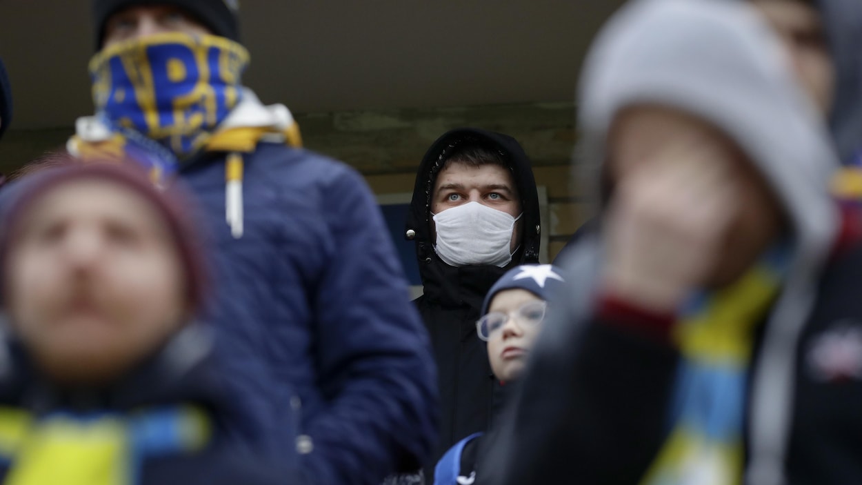Des supporteurs du FC Bate, dont un qui porte un masque protecteur, assistent à une rencontre.