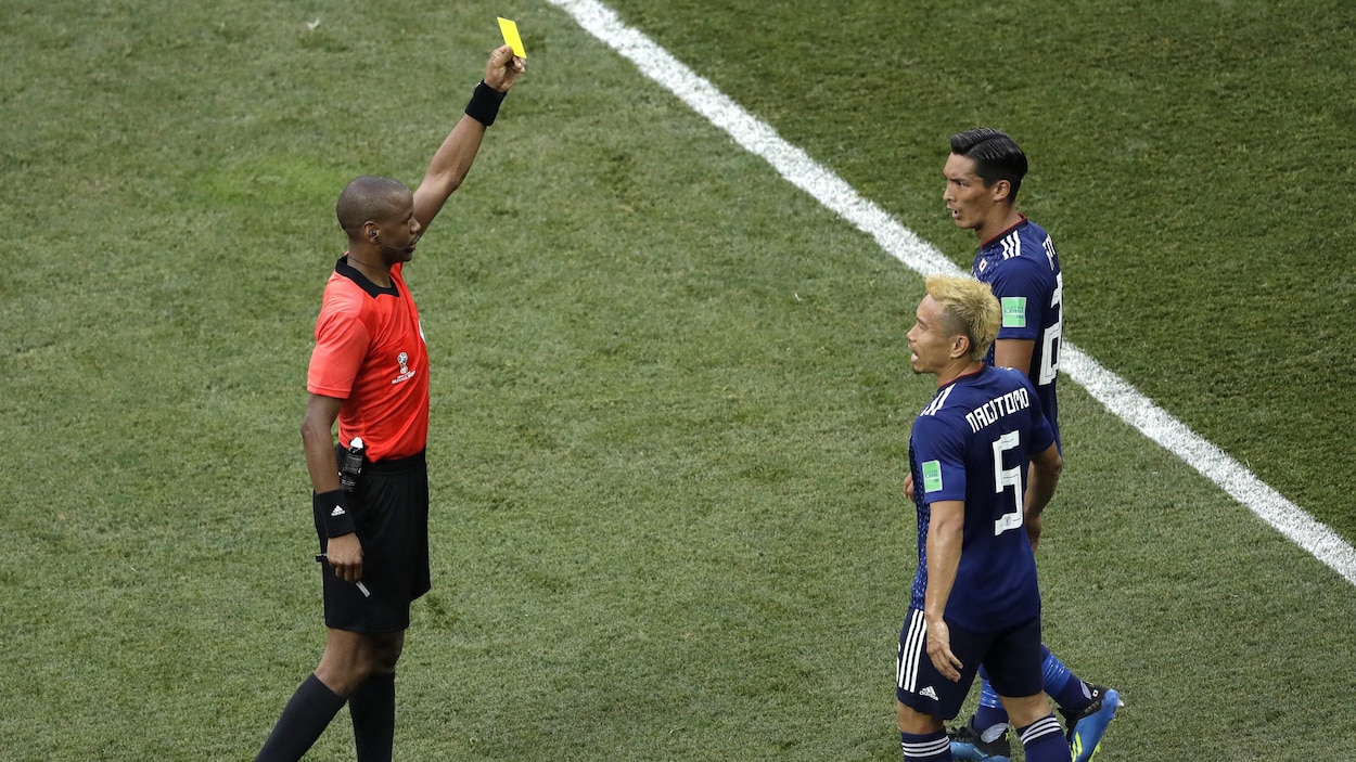 L'arbitre Janny Sikazwe (à gauche) montre un carton jaune au Japonais Tomoaki Makino (à droite) au cours du match entre le Japon et la Pologne.