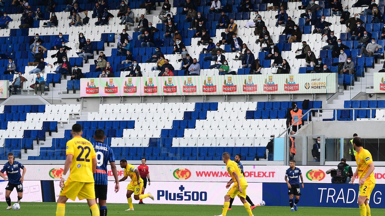 Des spectateurs éparpillés dans une tribune regardent un match de soccer.