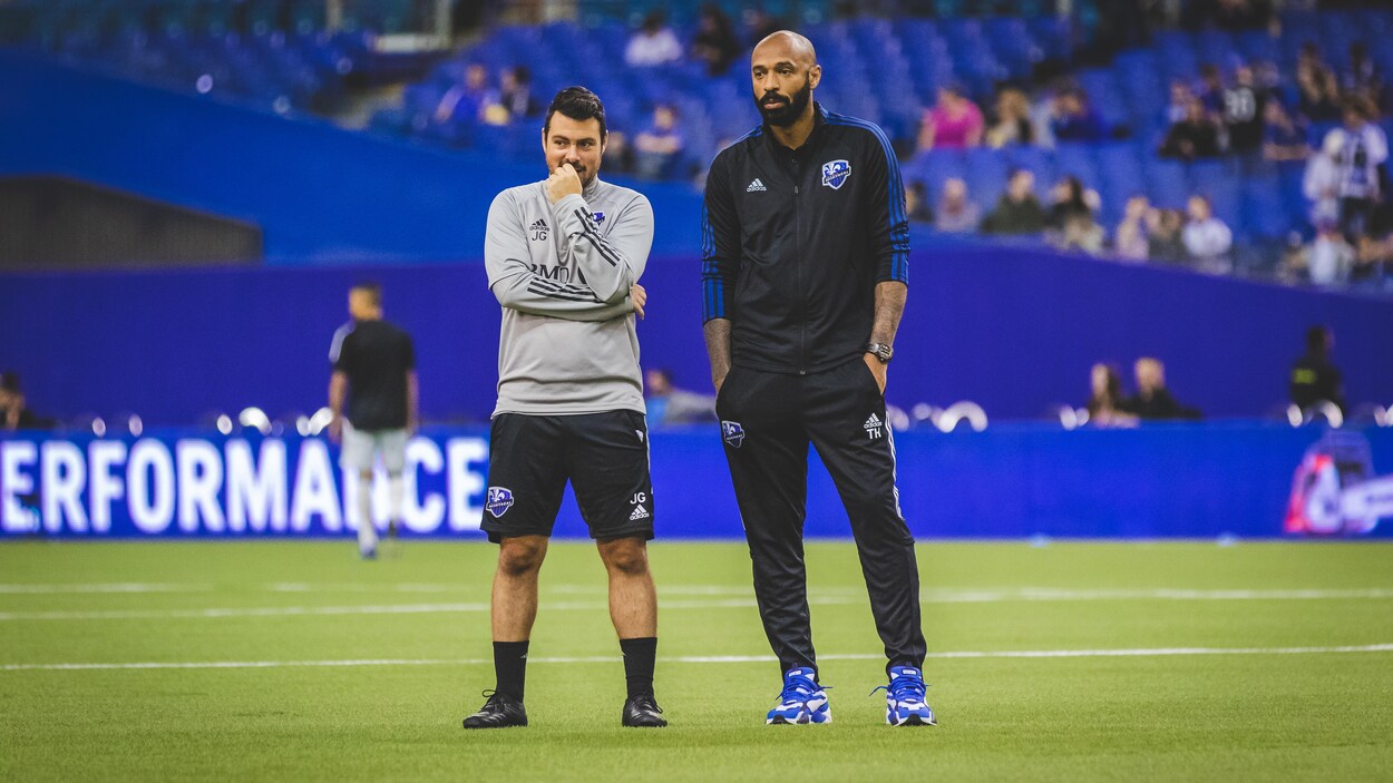 Il discute avec l'entraîneur Thierry Henry, la main devant son menton.
