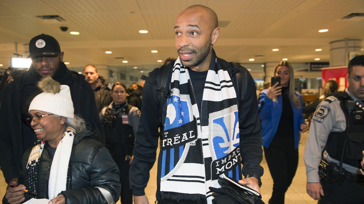 Il marche dans l'aéroport, une écharpe de l'Impact autour du cou.