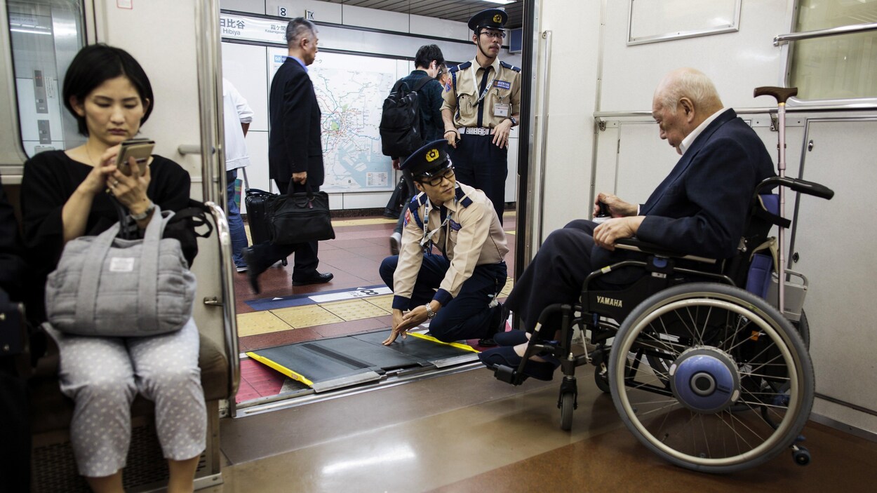 Une personne âgée japonaise est aidée à sortir du métro de Tokyo par deux employés.