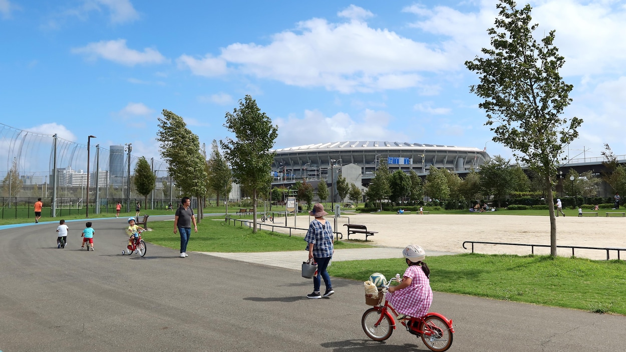 Des gens marchent devant un parc. Au loin, il y a un stade.