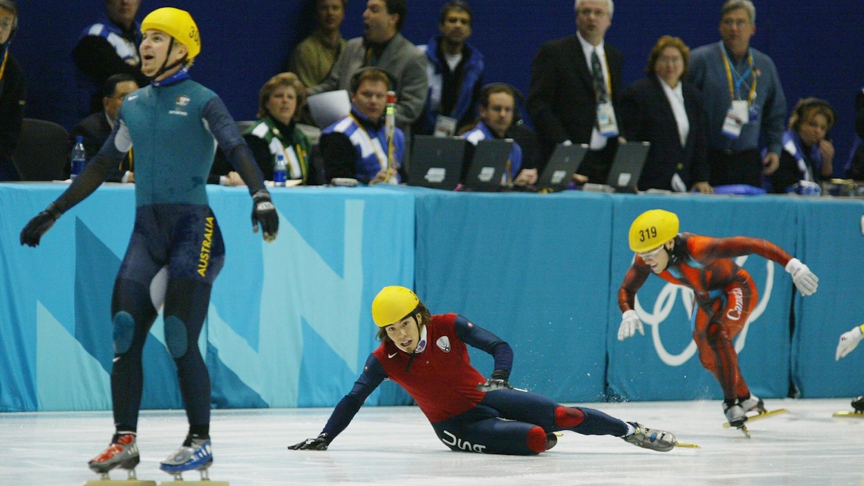 Il célèbre sa victoire, tandis qu'un patineur est étendu sur la glace et que l'autre se relève.