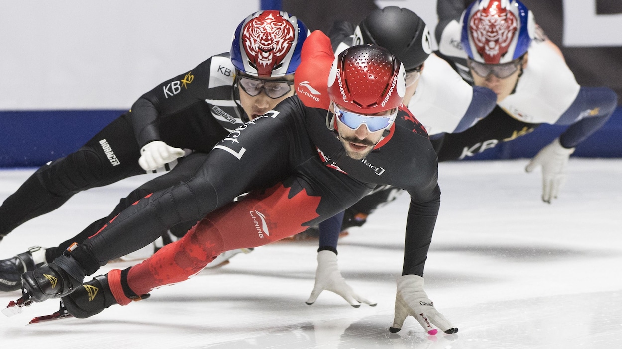 Il prend un virage, une main sur la glace, devant trois adversaires.