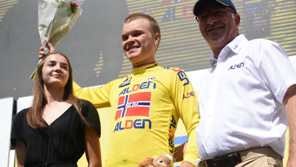 Il est sur le podium avec des fleurs et son maillot jaune.