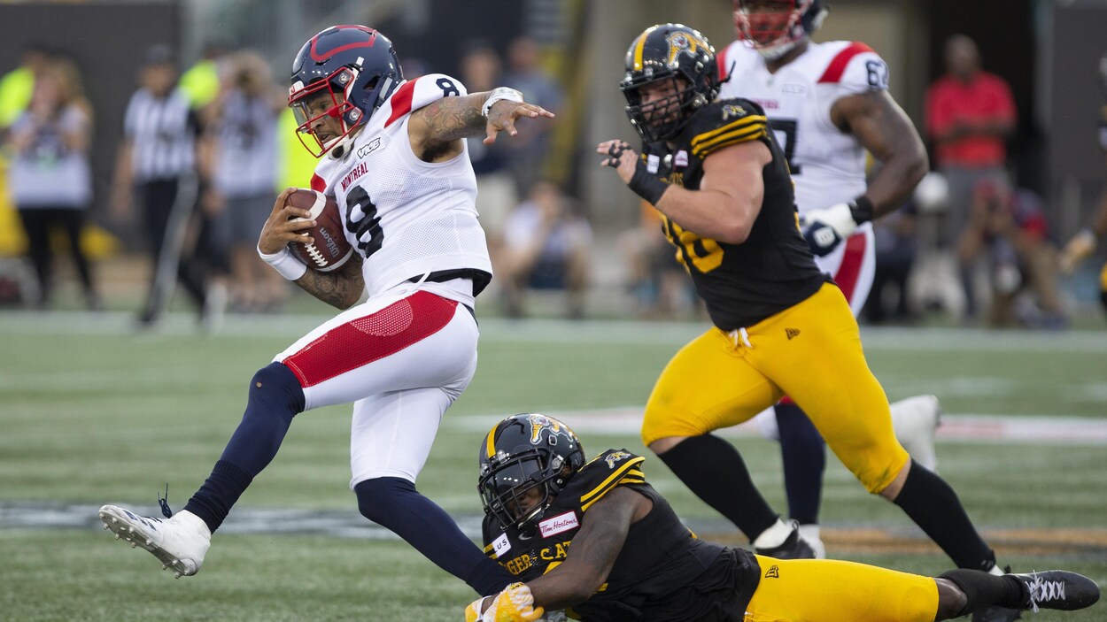 Vernon Adams fils (à gauche) est pourchassé par deux joueurs des Tiger-Cats.