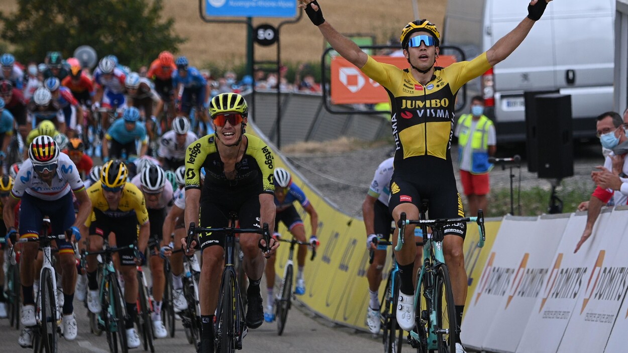 Il lève les bras en guise de victoire pendant que le peloton suit tout juste derrière.