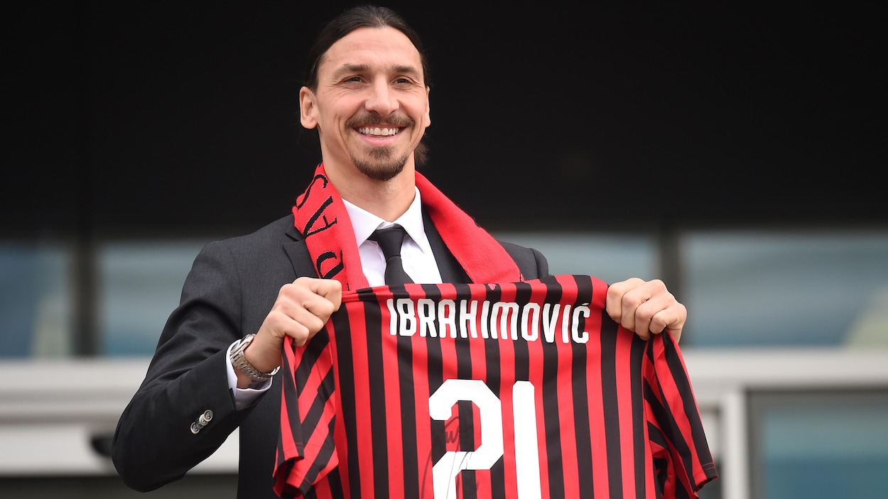 Il tient son maillot dans ses mains en souriant.