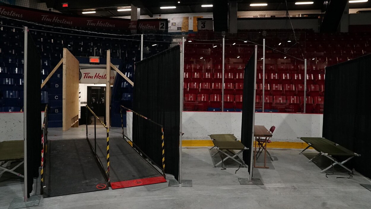 Un lit de camp installé devant des gradins vides dans un aréna.