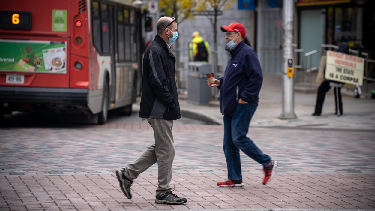 Deux hommes masquée se croisent en traversant une rue d'Ottawa.