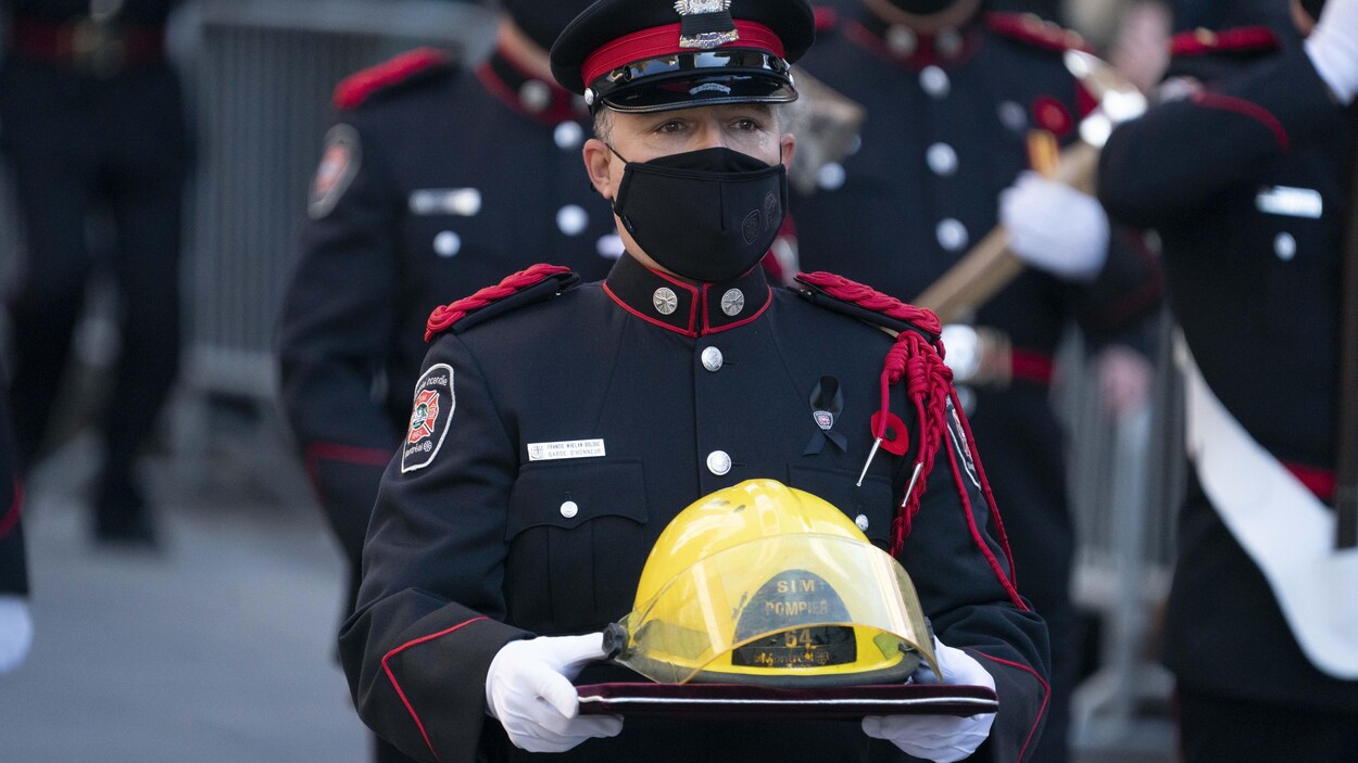 Un pompier en uniforme tient un casque jaune entre ses mains.