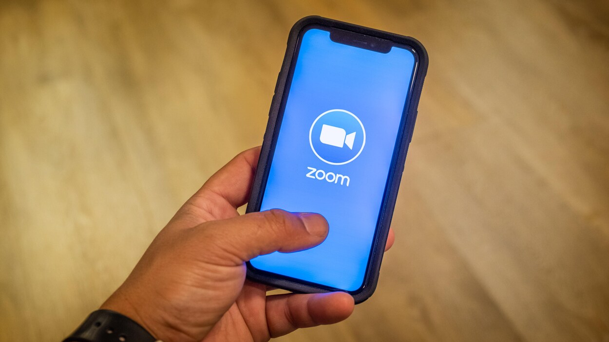 Une main tenant un téléphone avec l’application Zoom à l'écran.