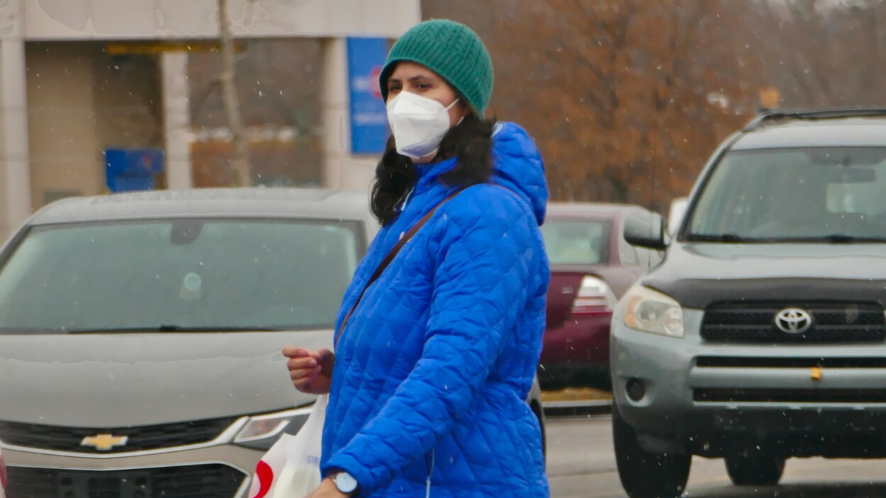 Une femme portant un masque traverse la rue en hiver.