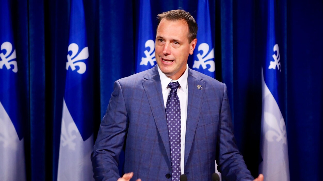 Jean-François Roberge en conférence de presse devant plusieurs drapeaux du Québec.