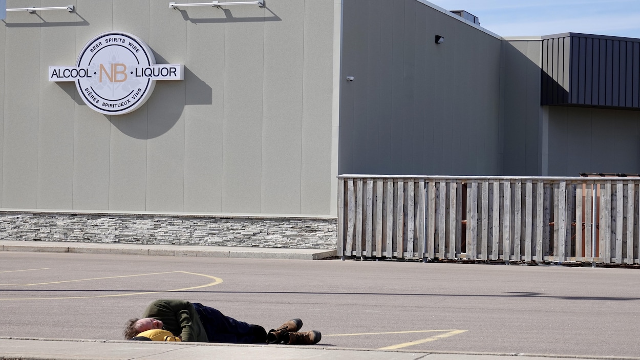 Un homme dort couché sur l'asphalte d'un terrain de stationnement.