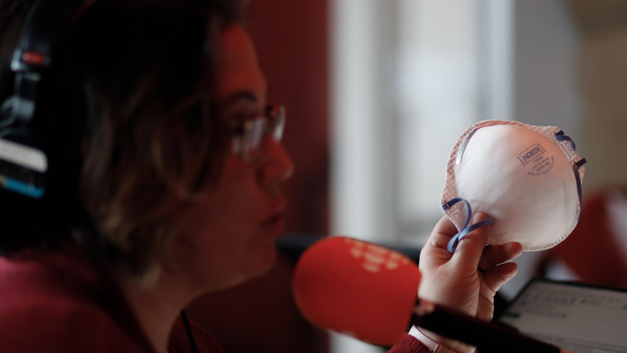 Une femme portant des lunettes montre un masque facial fait de papier servant à se protéger de potentielles infections.