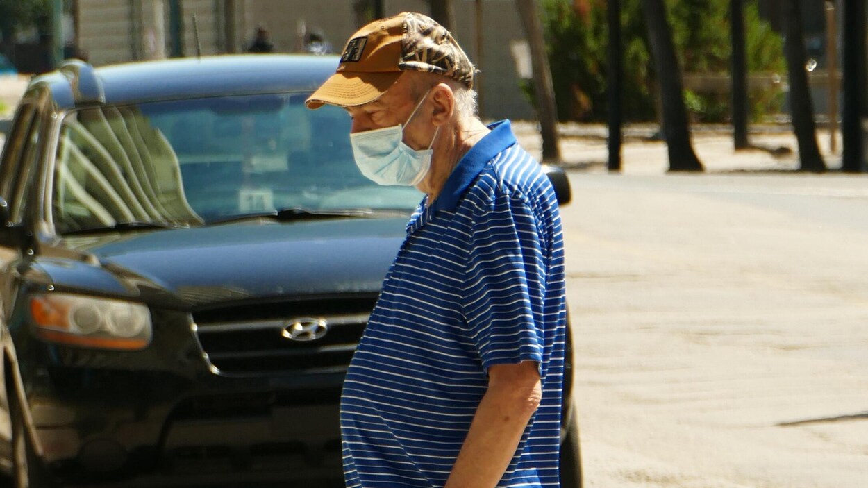 Un homme avec un masque devant une voiture.