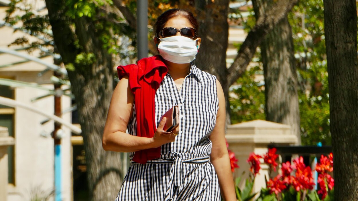 Une femme marche dans la rue avec un masque.