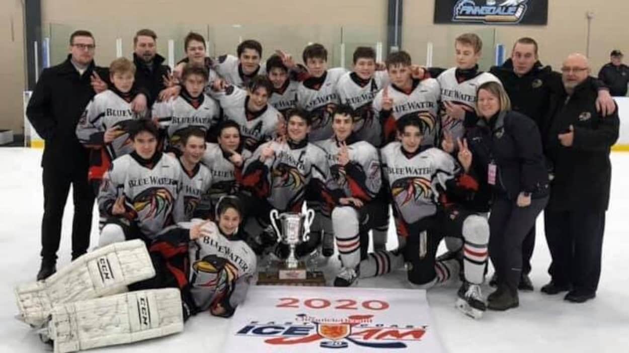 Une équipe de hockey masculine pose devant une bannière et un trophée.