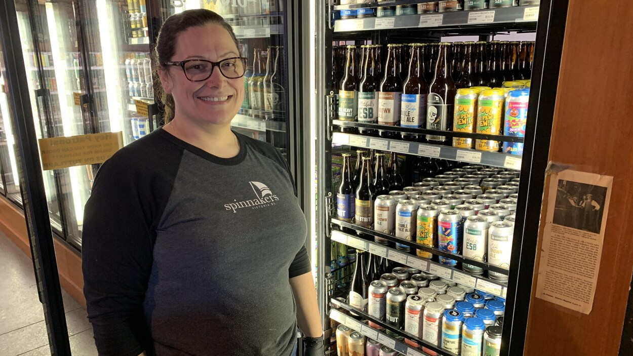La gérante pose devant des réfrigérateurs remplis de bouteilles et de canettes de bières.