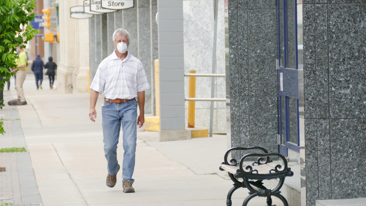 Un homme ayant les cheveux blancs et portant un masque marche dans les rues de Saskatoon.