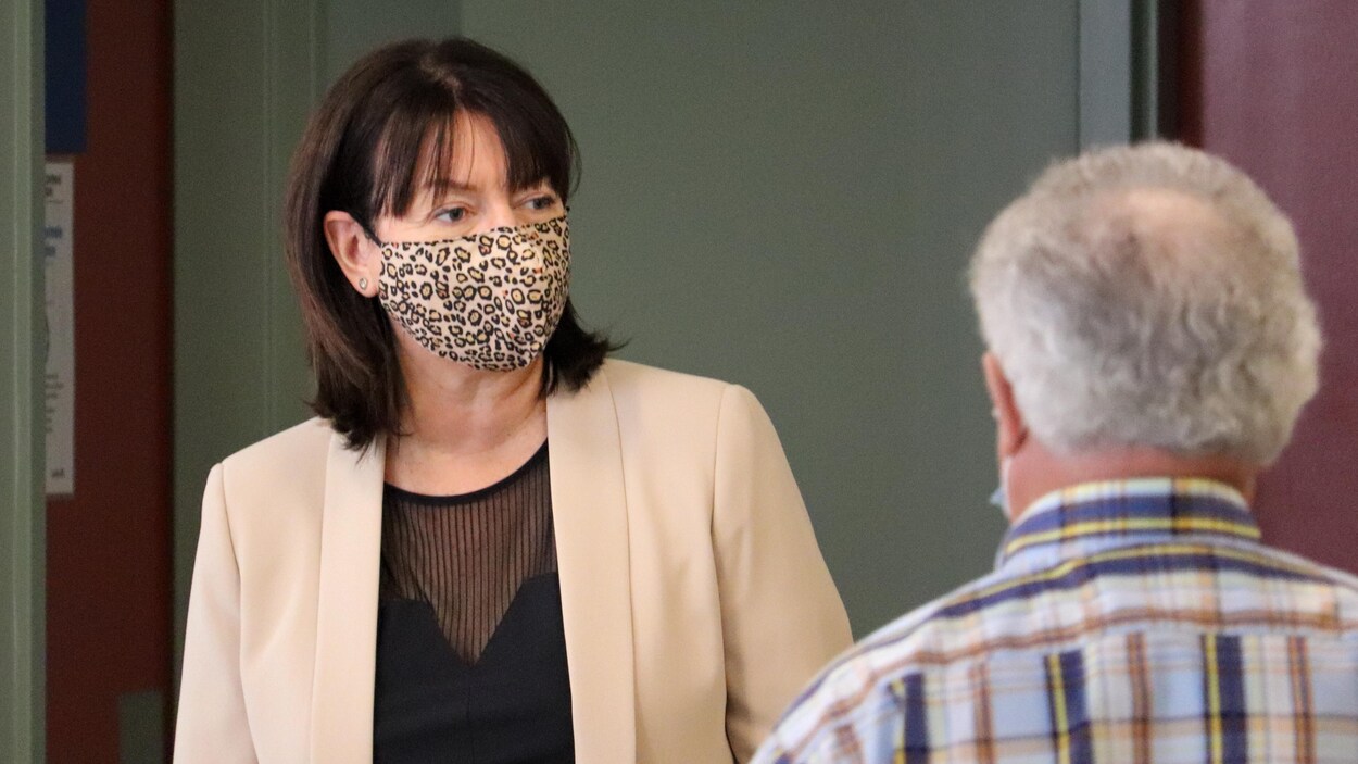 Nathalie Normandeau porte un masque avec un imprimé en léorpard. Elle porte aussi un veston beige. On la voit de face, à l'intérieur.