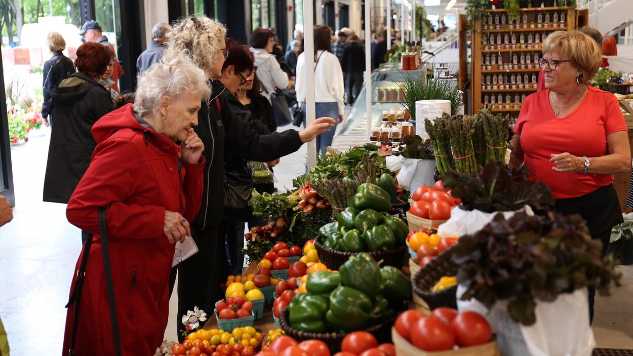 Des visiteurs devant un kiosque de fruits et légumes au Grand Marché de Québec.