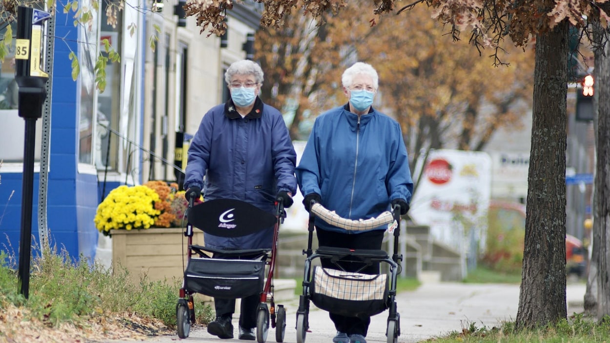 Deux personnes aînés portant un masque marchent sur le trottoir de le rue St-George, à Moncton au Nouveau-Brunswick.