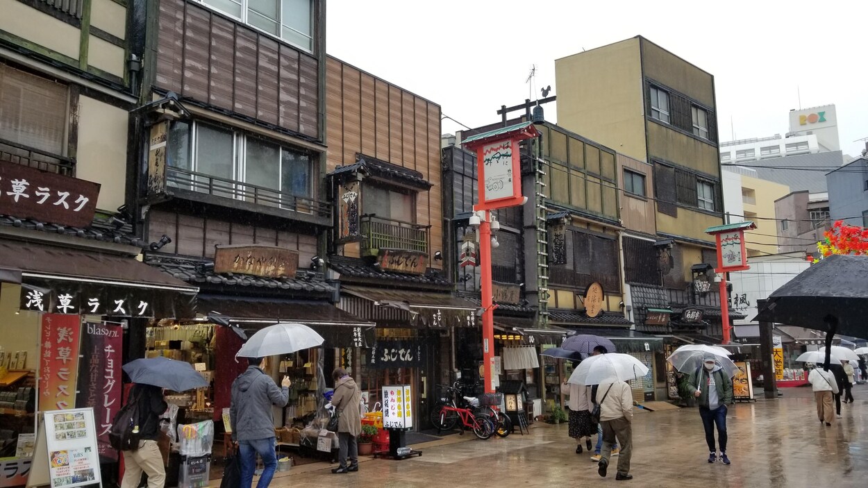 Des habitants font leurs emplettes muni d'un parapluie.