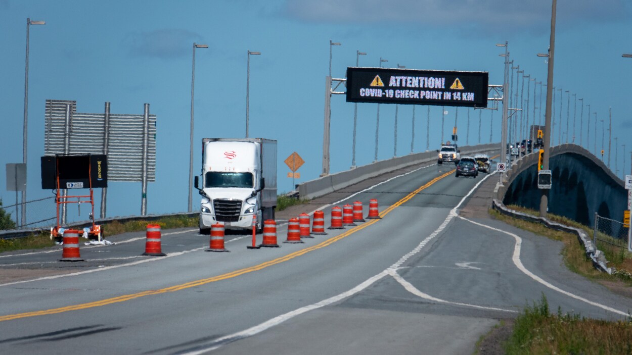 Un camion sort du pont. En haut du pont, un tableau d'affichage numérique donne des informations sur la COVID-19.