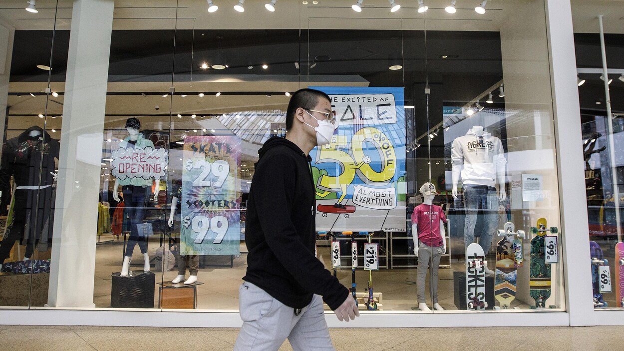 Un homme marche devant un magasin avec un masque.