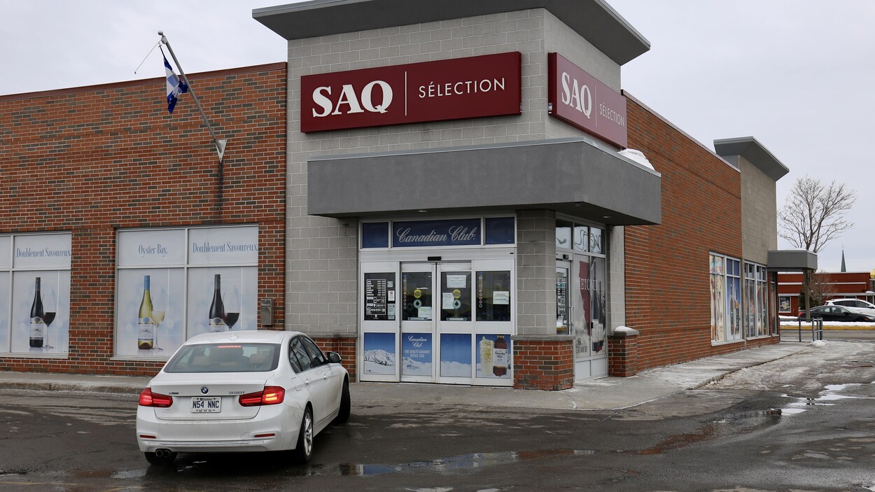 Une voiture blanche dans le stationnement d'une succursale de la SAQ fermée en raison du passage d'une personnes présentant es symptômes s'apparentant à ceux de la COVID-19.
