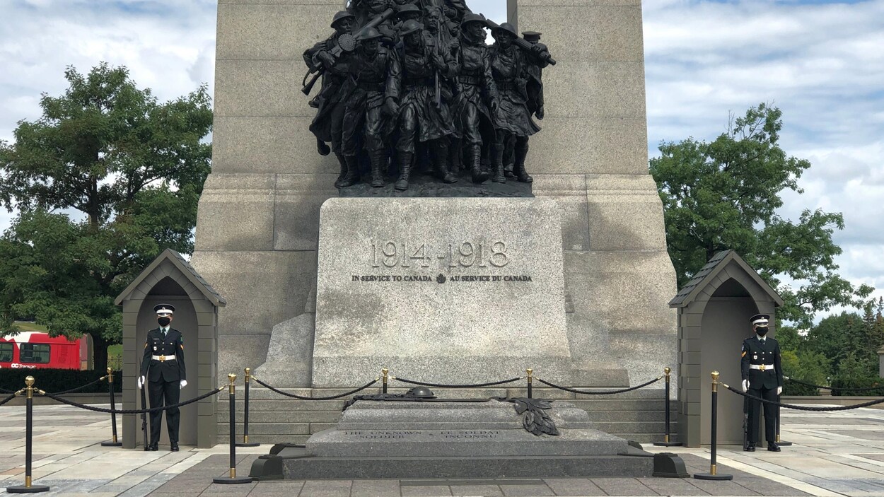 Deux soldats portant un masque sont placés sur les côtés du Monument commémoratif de guerre.