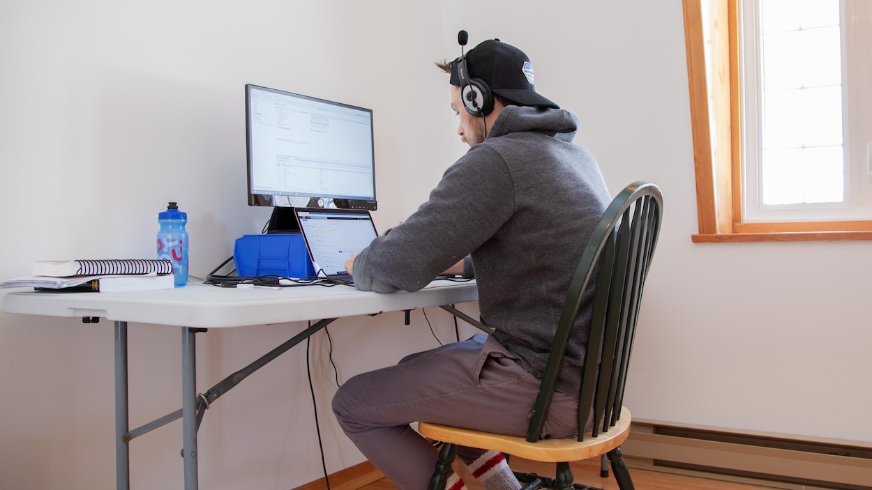 Un homme qui porte un casque d'écoute fixe son écran ordinateur.
