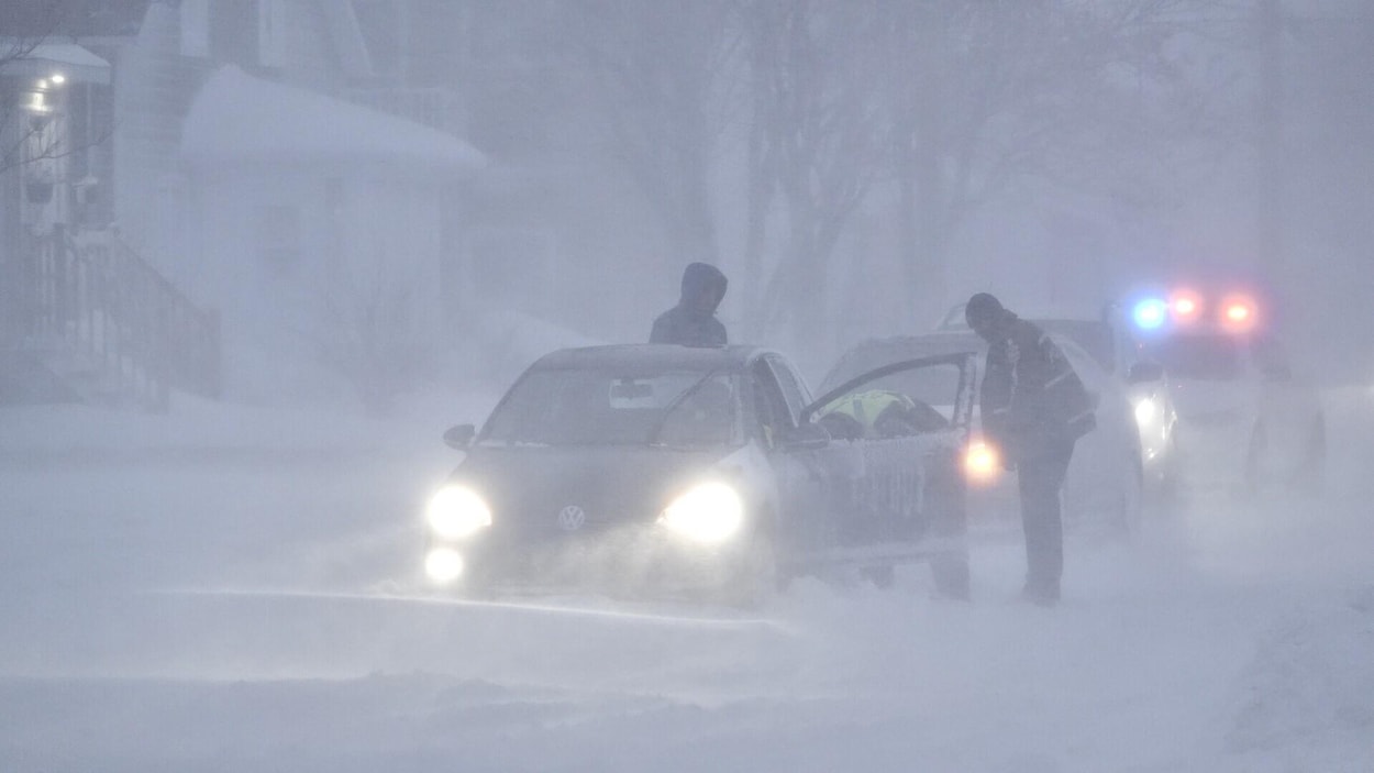 Des policiers viennent en aide à un automobiliste en difficulté sur une rue recouverte de neige.