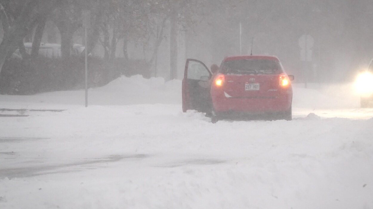 Le conducteur d'une voiture ouvre sa porte alors que son véhicule semble coincé dans un petit banc de neige pendant une tempête.
