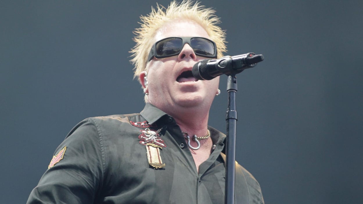 Le chanteur du groupe The Offspring, sur scène, en train de chanter dans un micro.
