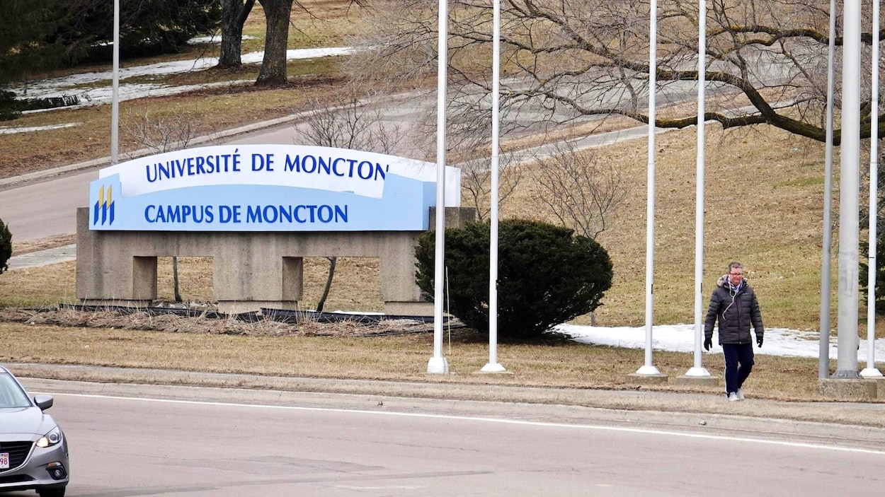 Une passante devant l'enseigne du campus de Moncton.