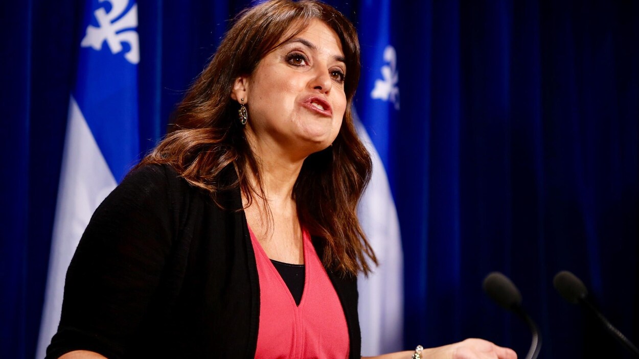 Véronique Hivon lors d'une conférence de presse; elle porte un chandail noir par-dessus un haut de couleur rose